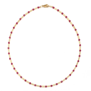 Detail view of a handmade necklace with red faceted beads and gold metal tubes in circular layout