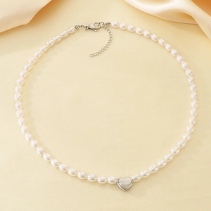 Detail of elegant pearl necklace with silver heart pendant on beige silk fabric background