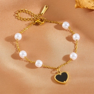 Détail du bracelet en acier doré avec pendentif cœur noir et perles blanches