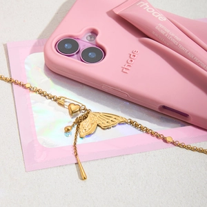 Flat lay of gold butterfly pendant necklace with pink rhode phone case and lip tint
