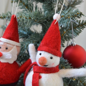 Handmade wool felt snowman and Santa Claus ornaments hanging on a lush green Christmas tree