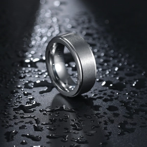 Men's brushed titanium steel ring with central groove on a dark water-droplet surface