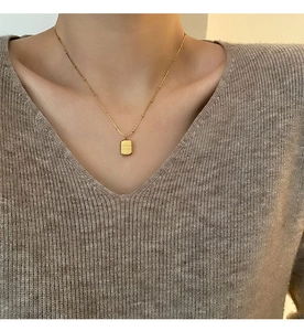 Detailed view of a gold square letter pendant necklace worn on a brown knit sweater