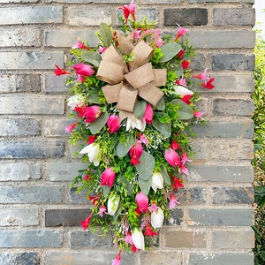 Pink tulip floral swag with greenery and burlap bow on a rustic brick wall