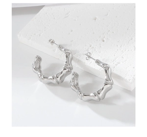 Macro shot of silver bamboo-style C-shaped hoop earrings on a textured stone stand