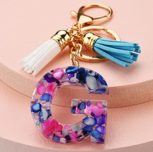 Detail of resin letter G keychain with colorful stone flakes and blue silk tassels