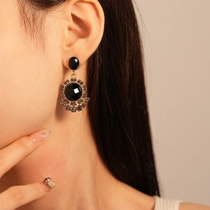 Close-up of retro black gemstone drop earring with gold floral frame on a model