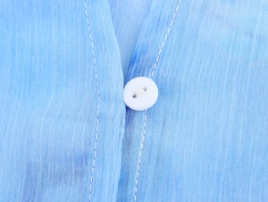 Dettaglio della trama del tessuto chiffon celeste e del bottone bianco sulla camicia
