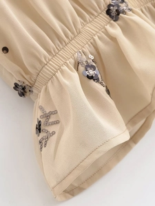 Détail d'une blouse en mousseline beige avec paillettes noires et smocks froncés