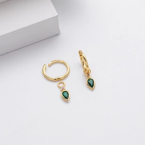 Macro shot of gold hoop earrings with green teardrop zircon charms on minimalist blocks