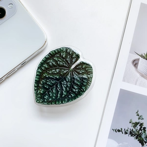 Detail shot of heart-shaped phone grip featuring deep green leaf texture on white desk