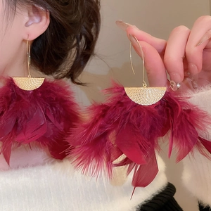 Detailed close-up of large burgundy feather tassel earrings with textured gold accents