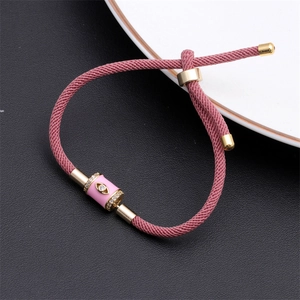 Macro shot of pink braided rope bracelet with gold evil eye charm and white zircon