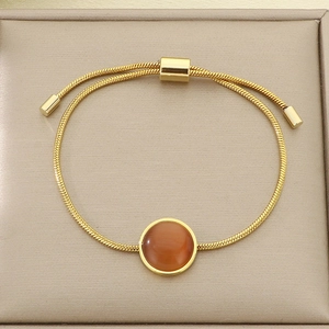 Détail d'un bracelet maille serpent dorée orné d'une pierre naturelle ronde ambrée