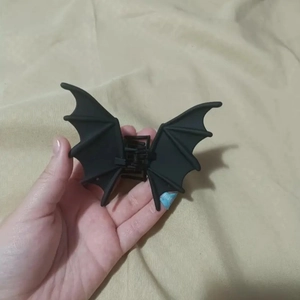 Close-up of matte black bat wing hair claw clip held by hand for Halloween punk style
