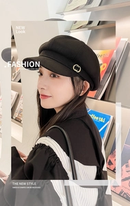 Close-up of a stylish black newsboy hat featuring a golden metal emblem on the side