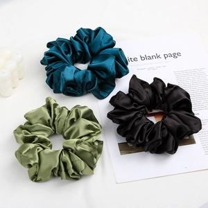 Close-up of silk satin scrunchies in navy, olive, and black on a minimalist lifestyle setting
