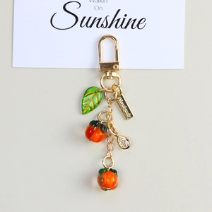 Macro shot of orange persimmon fruit keychain with green leaf and handmade metal tag