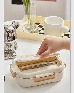 Macro detail of a beige and gold bento box set with stainless steel utensils and a lunch lid