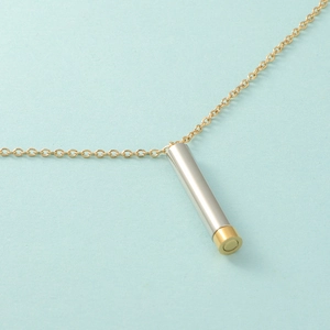 Macro detail of the golden chain and two-tone silver and gold cylindrical pendant