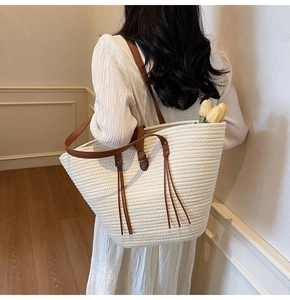 Detail of woven tote bag with leather handles and decorative tassel in casual setting