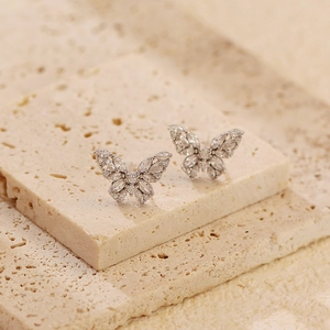 Macro shot of silver butterfly earrings with sparkling crystals on beige stone base