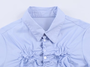 Close-up of light blue poplin shirt featuring elastic pleats and pearl buttons details