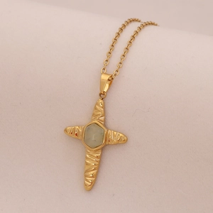 Detailed shot of gold cross necklace with hexagonal gemstone and hammered texture