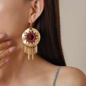 Detail view of gold circular earrings with red woven accents and long fringe tassels
