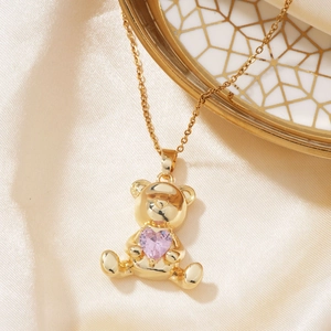 Golden teddy bear necklace with a pink heart-shaped zircon pendant on silk fabric