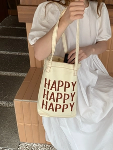 Detail of beige canvas tote bag with brown HAPPY text print shown in use