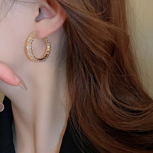 Close-up of elegant gold C-shaped hoop earrings with zircon stones worn by a model
