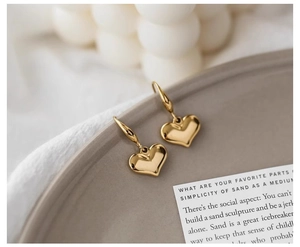 Close-up of golden polished 3D heart-shaped drop earrings on minimalist tray