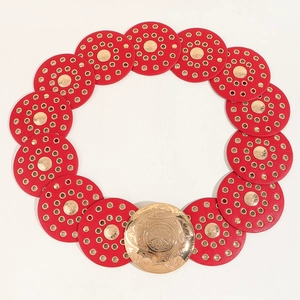 Detail of red leather belt with gold round eyelets and ornate carved buckle closure