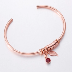 Detailed macro view of rose gold leaf bracelet with a vibrant red round gemstone charm
