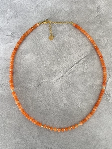 Detailaufnahme einer orangefarbenen Steinkette mit goldenen Zwischenstücken auf Stein