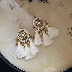 Detail of bohemian gold flower earrings with white cotton tassels on a decorative tray