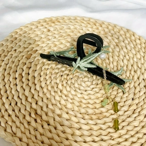 Bamboo style hair claw clip with green leaf embroidery and golden tassel on woven mat
