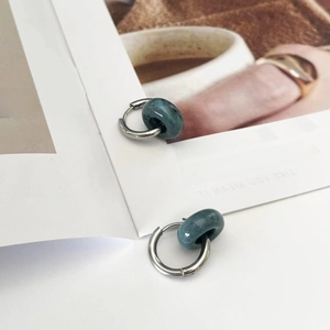 Close-up of silver steel hoop earrings with dark teal natural stone beads on a magazine