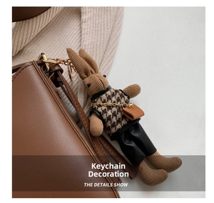 Detail of a brown knitted rabbit doll charm with houndstooth vest on a leather bag