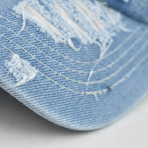 Detail of light blue washed denim cap featuring distressed rips and white stitching details