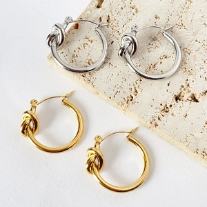 Detail of 316L knot hoop earrings in gold and silver finish on stone background