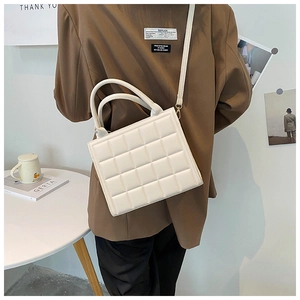 Detail of cream quilted square handbag worn with dark brown suit blazer