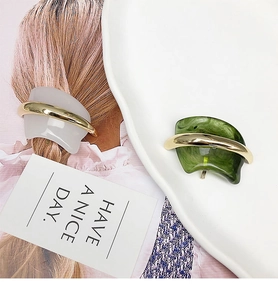 Detail of white and green resin hair clips with gold metal accents on a model and tray