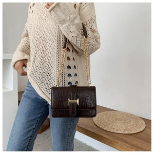 Detail of dark brown crocodile pattern bag with a gold chain strap and metal buckle