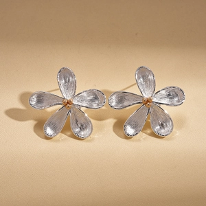 Macro detail of silver flower stud earrings with brushed texture and golden bead center