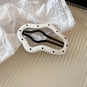 Close-up of wavy white hair clip with black polka dots and faux leather stitching