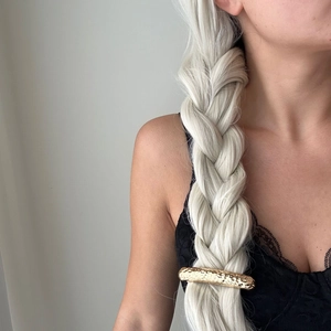Close-up of hammered gold metal hair clip securing a thick silver blonde braid