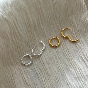 Detailed top view of minimalist gold and silver hoop earrings on textured beige fabric