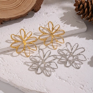 Detailed view of hollow floral earrings in gold and silver finish on textured stone